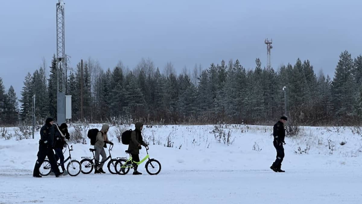 Kolme polkupyörää työntävää ihmistä ja kaksi rajavartijaa itärajalla Kuhmossa 20.22.2023.
